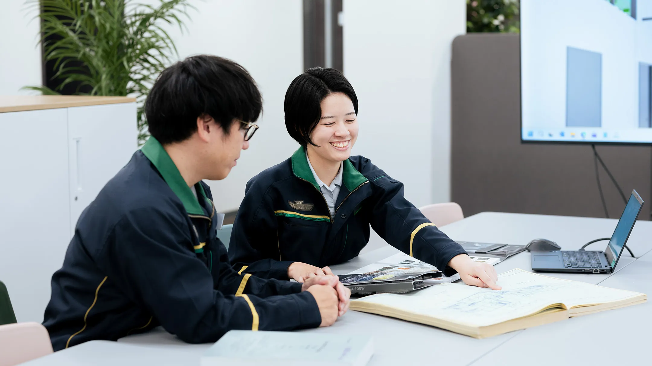 オフィスのデスクで、同僚と資料を見ながら、笑顔で打ち合わせをする社員の写真